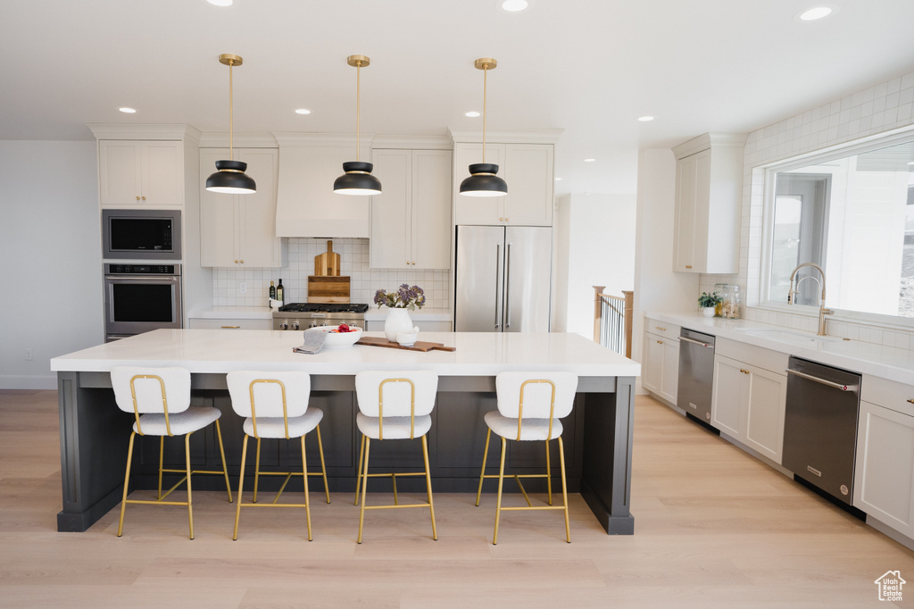 Kitchen with built in appliances, a sink, decorative backsplash, a spacious island, and light wood finished floors