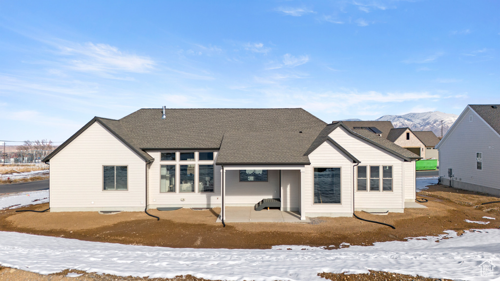 Snow covered rear of property with a patio and roof with shingles
