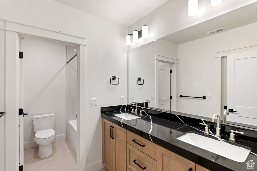 Bathroom with double vanity, toilet, tile patterned flooring,  shower combination, and baseboards