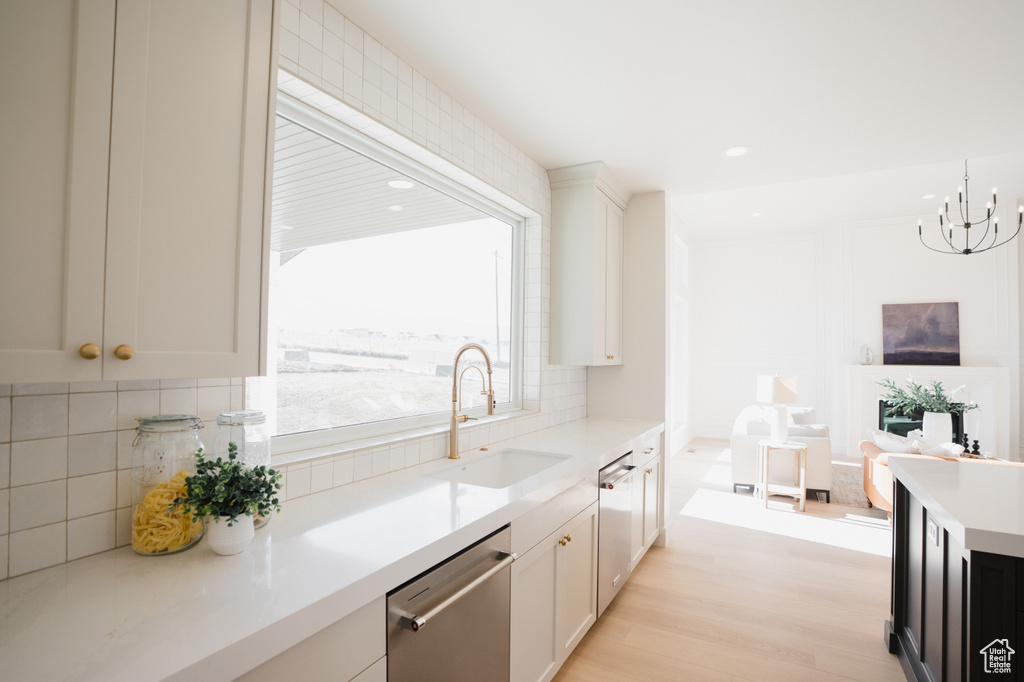 Kitchen featuring stainless steel dishwasher, a sink, light countertops, tasteful backsplash, and a chandelier