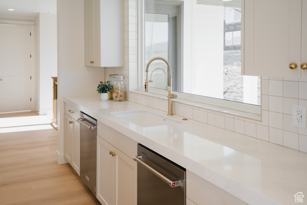 Kitchen featuring a sink, stainless steel dishwasher, tasteful backsplash, light countertops, and light wood finished floors
