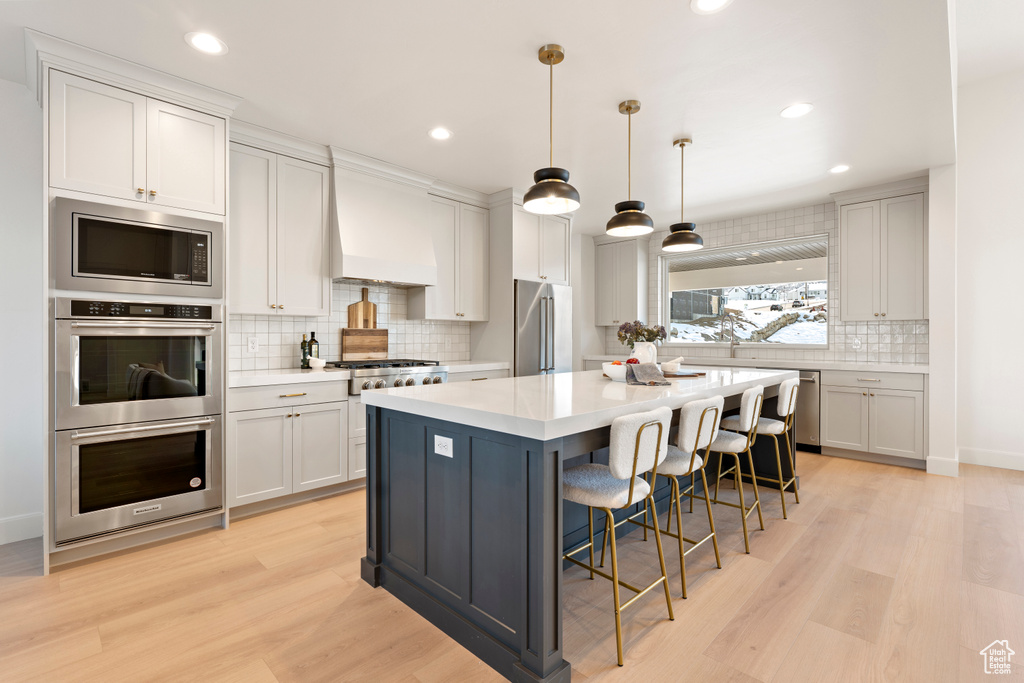 Kitchen featuring appliances with stainless steel finishes, tasteful backsplash, light wood finished floors, a kitchen breakfast bar, and recessed lighting