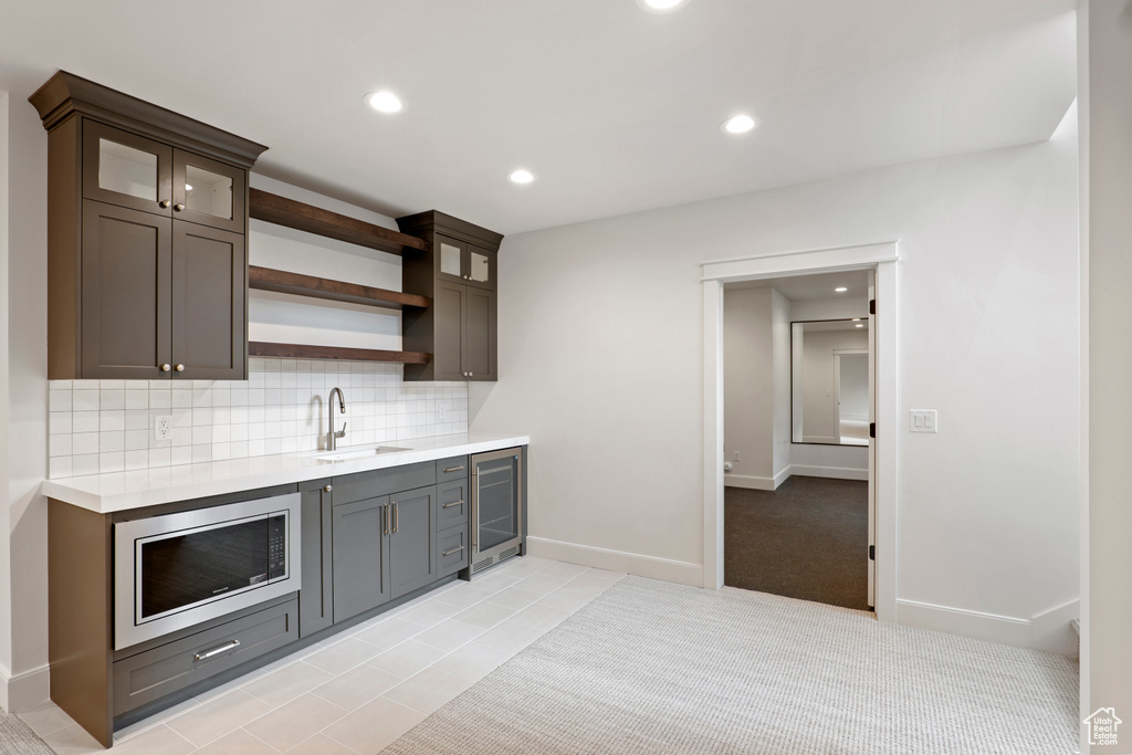 Bar area featuring stainless steel microwave, beverage cooler, a sink, backsplash, and recessed lighting