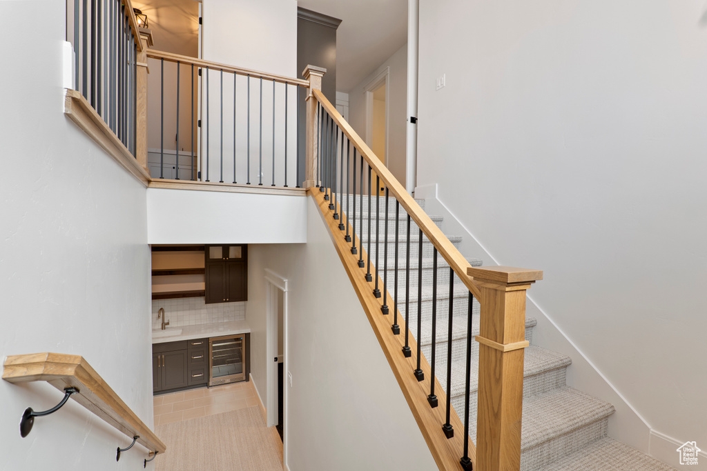 Stairs featuring wine cooler, bar with sink, and tile patterned floors