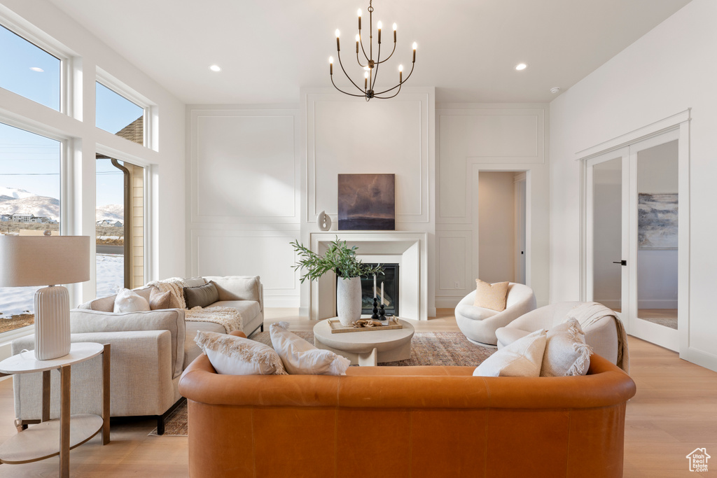 Living area featuring light wood finished floors, a decorative wall, a chandelier, french doors, and a fireplace