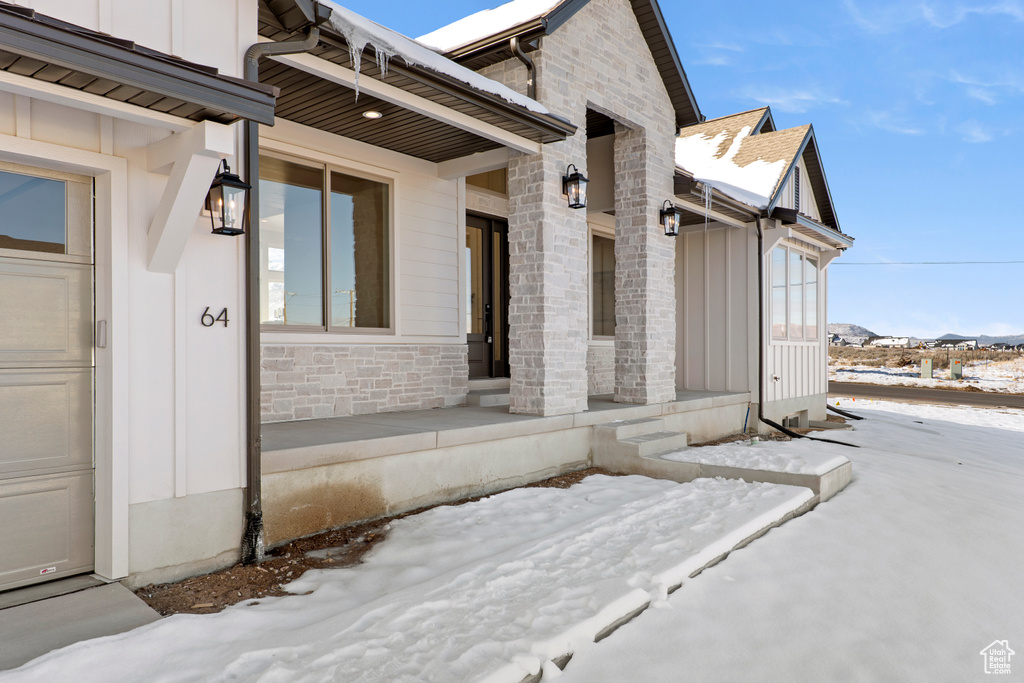 Snow covered property entrance featuring stone siding, board and batten siding, and a garage