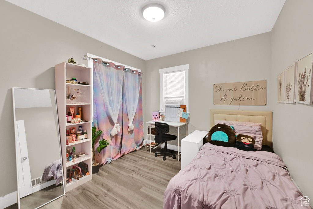 Bedroom with light wood-style floors, an office area, and a textured ceiling