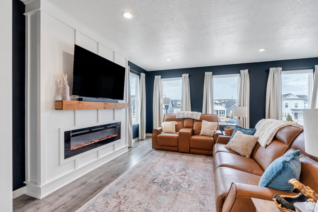Living room featuring a textured ceiling, light wood-style floors, a glass covered fireplace, recessed lighting, and baseboards