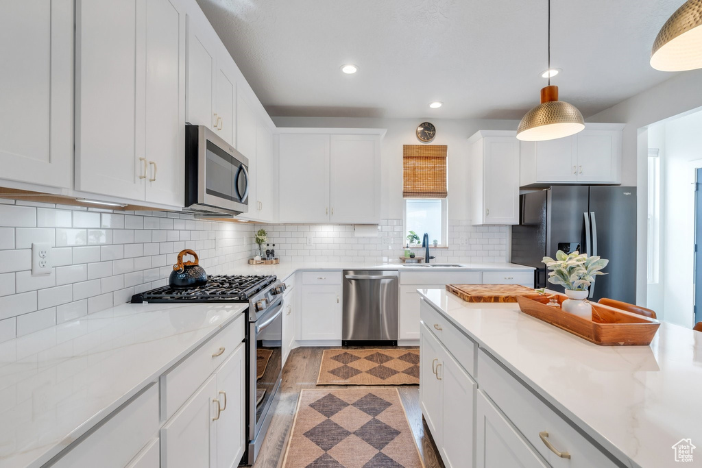 Kitchen with stainless steel appliances, a sink, white cabinets, pendant lighting, and recessed lighting