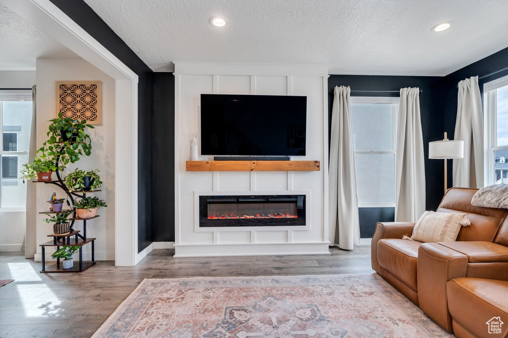 Living room featuring wood finished floors, a textured ceiling, a glass covered fireplace, recessed lighting, and baseboards