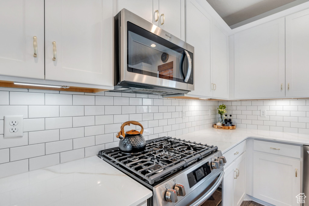 Kitchen featuring appliances with stainless steel finishes, white cabinetry, light stone counters, and backsplash