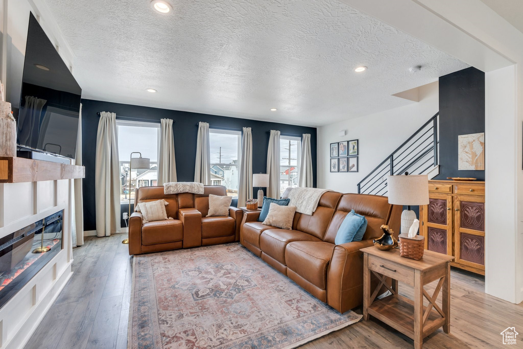 Living area with a textured ceiling, light wood-style flooring, stairway, a glass covered fireplace, and recessed lighting