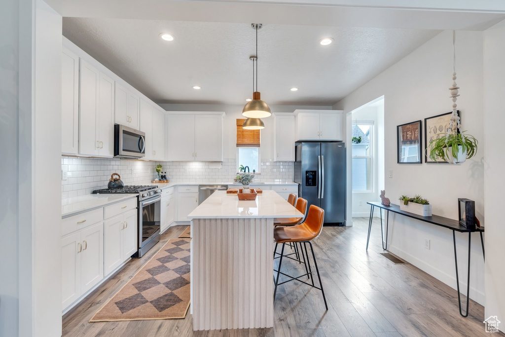 Kitchen featuring stainless steel appliances, a kitchen breakfast bar, tasteful backsplash, light countertops, and light wood-type flooring