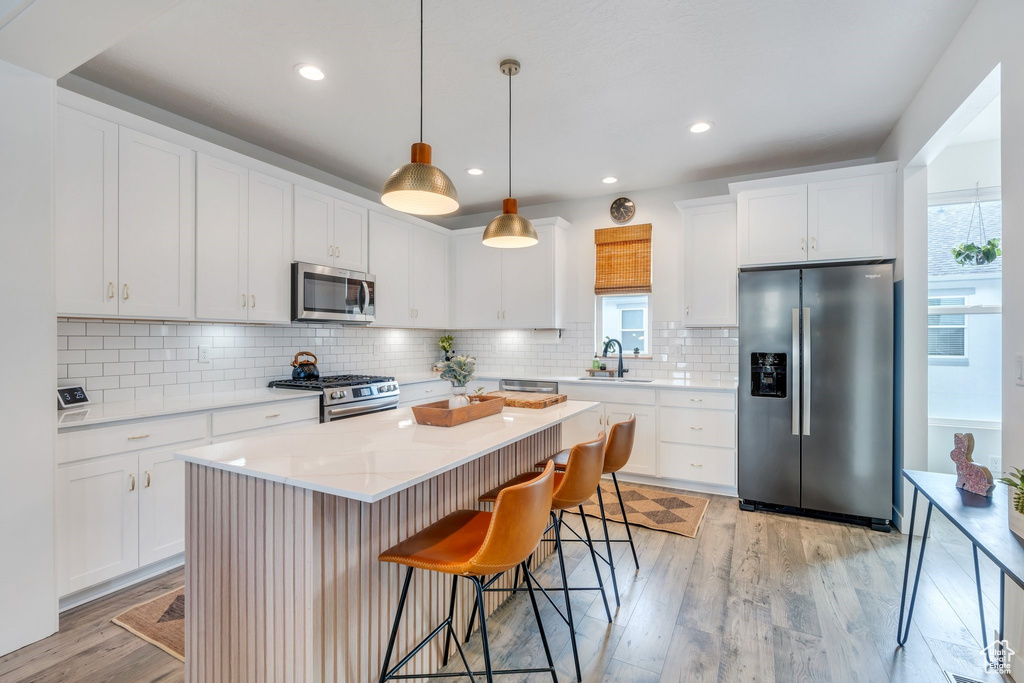 Kitchen featuring stainless steel appliances, healthy amount of natural light, light wood-style floors, a kitchen breakfast bar, and recessed lighting