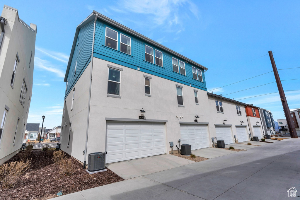 Back of property featuring stucco siding, an attached garage, central AC, and driveway