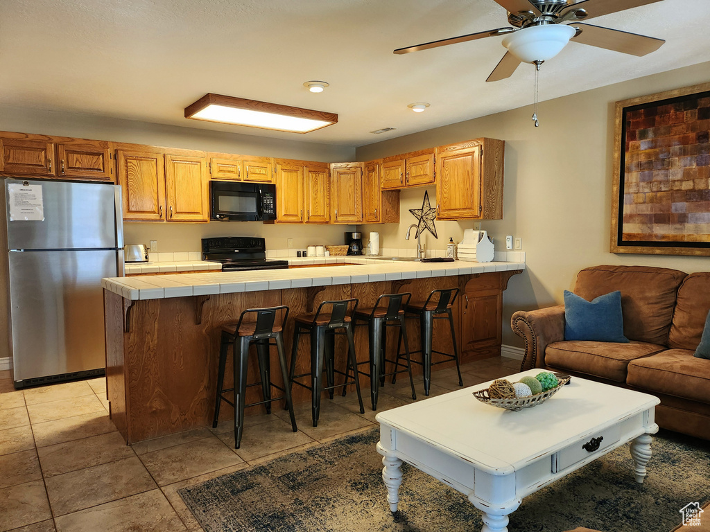 Kitchen featuring black appliances, tile counters, a peninsula, a breakfast bar, and light tile patterned floors