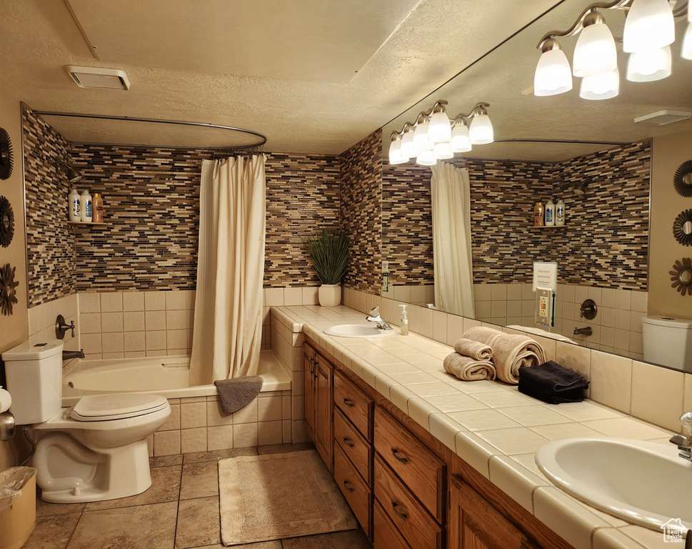 Full bathroom featuring double vanity, tiled shower / bath, and a textured ceiling