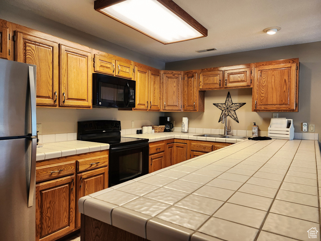 Kitchen with black appliances, tile countertops, and brown cabinetry
