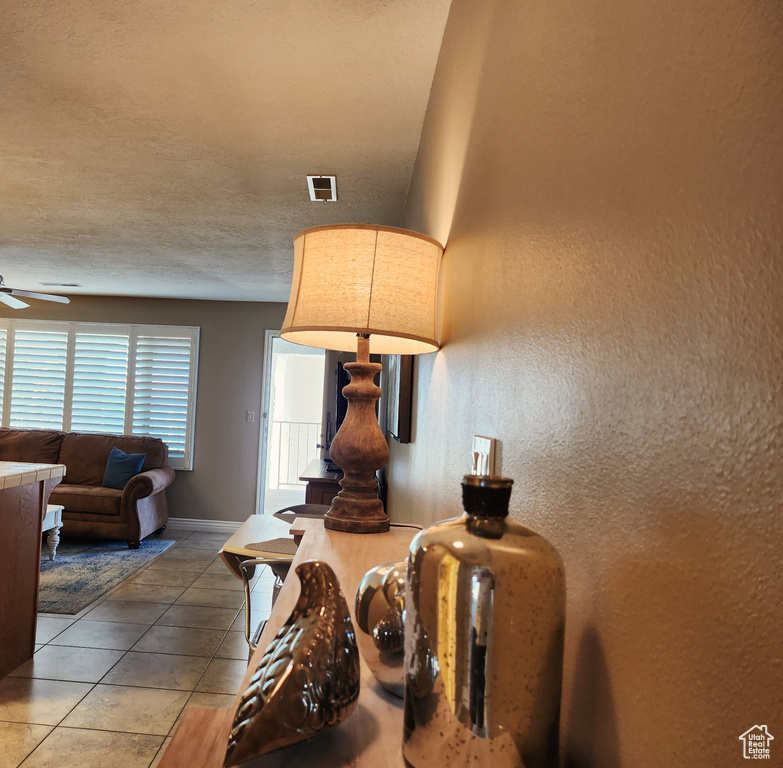 Living area with light tile patterned floors, ceiling fan, and a textured wall