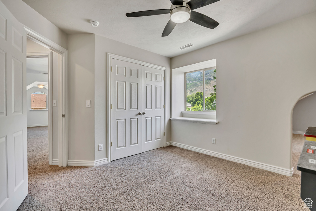 Unfurnished bedroom with carpet floors, arched walkways, a closet, a ceiling fan, and baseboards