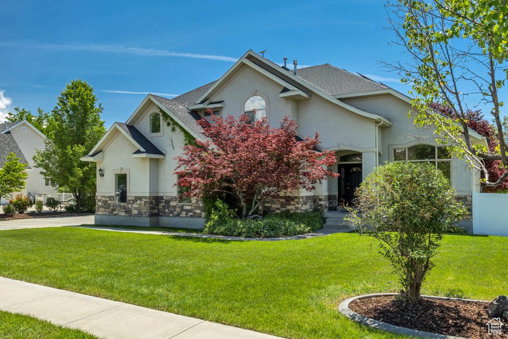 View of front of house featuring stucco siding, stone siding, a front lawn, and a shingled roof