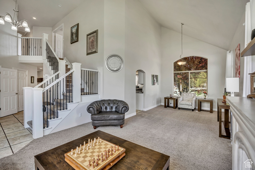 Carpeted living area with high vaulted ceiling, stairs, a chandelier, baseboards, and arched walkways