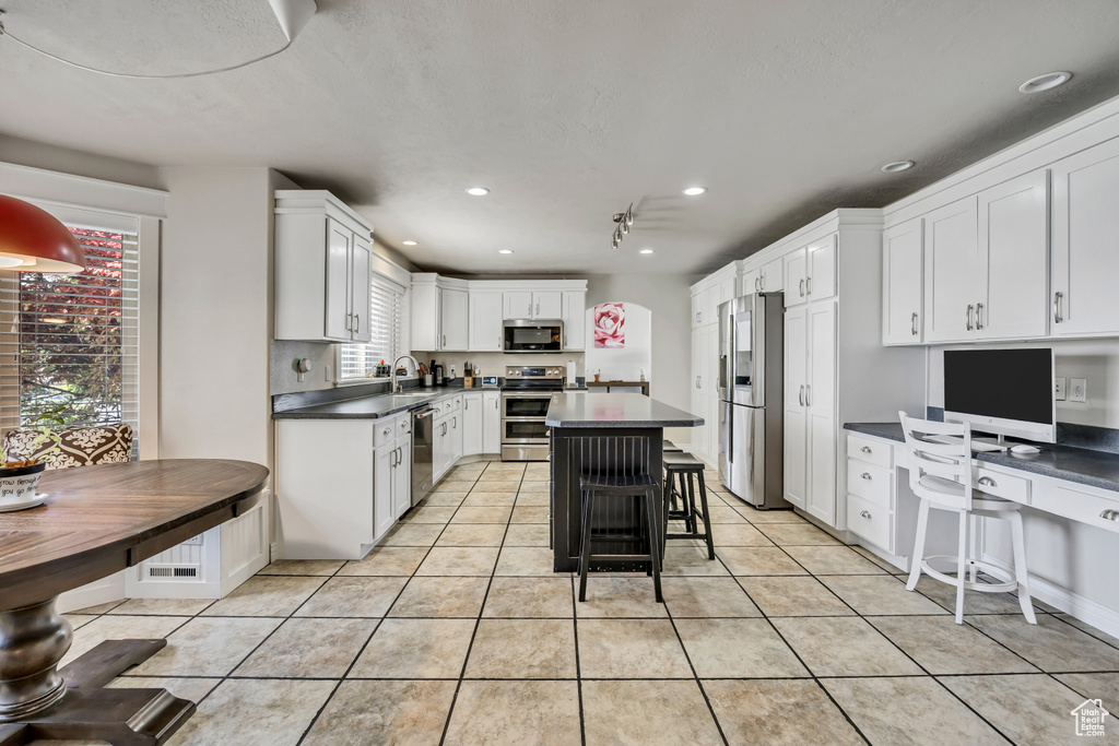 Kitchen featuring stainless steel appliances, dark countertops, white cabinetry, light tile patterned floors, and a center island