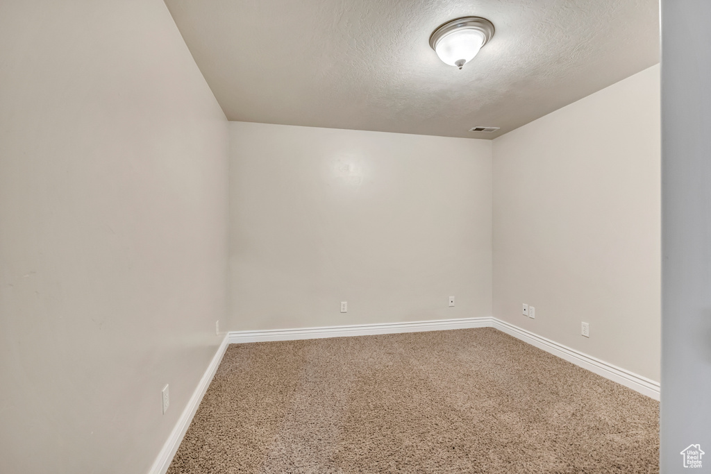 Carpeted empty room with a textured ceiling and baseboards