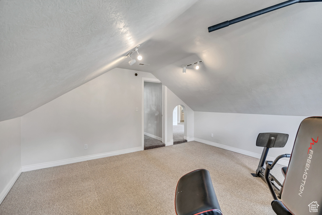Exercise room with track lighting, vaulted ceiling, baseboards, carpet, and a textured ceiling