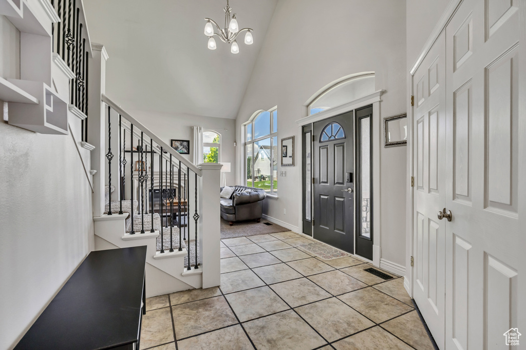 Foyer with high vaulted ceiling, stairs, a chandelier, tile patterned floors, and baseboards