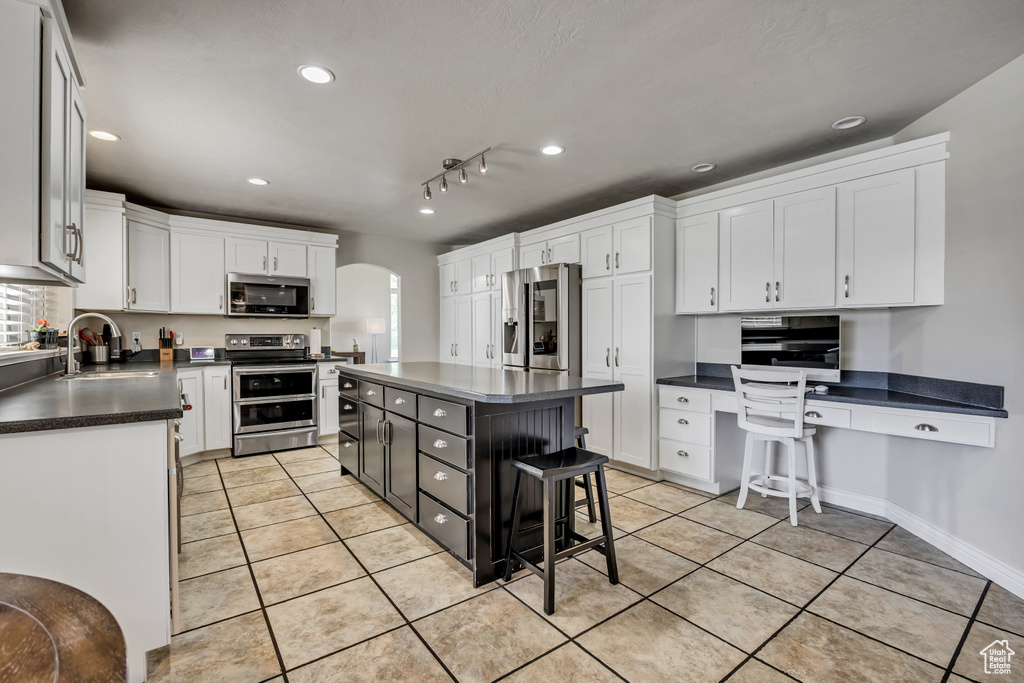Kitchen with stainless steel appliances, dark countertops, arched walkways, light tile patterned flooring, and recessed lighting