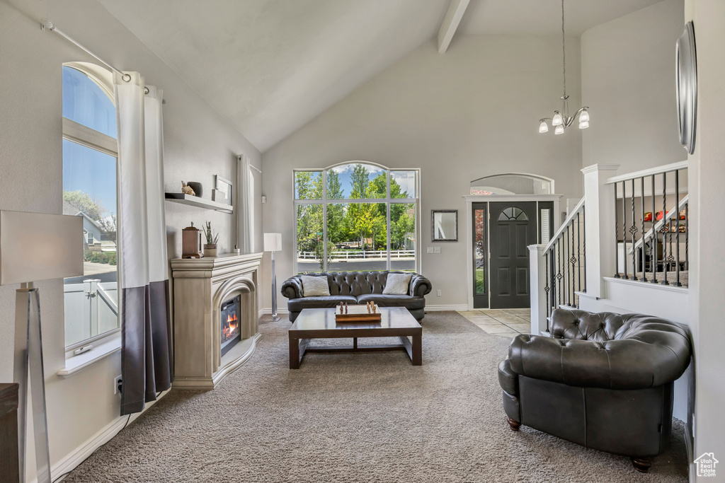 Living room featuring high vaulted ceiling, beam ceiling, a glass covered fireplace, carpet, and a chandelier