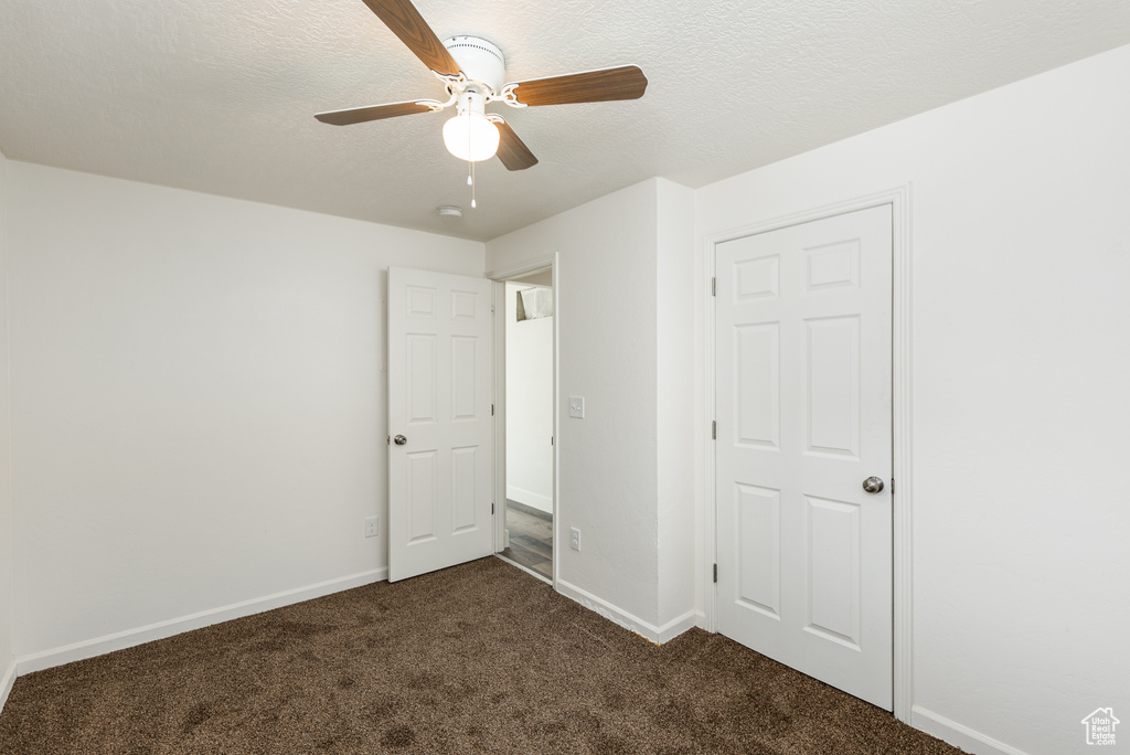 Unfurnished bedroom with dark colored carpet, baseboards, a textured ceiling, and a ceiling fan