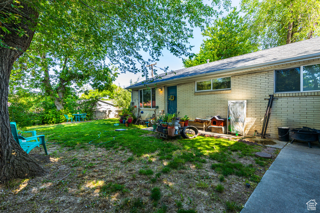 Rear view of house with brick siding, a lawn, a shingled roof, and an outdoor fire pit