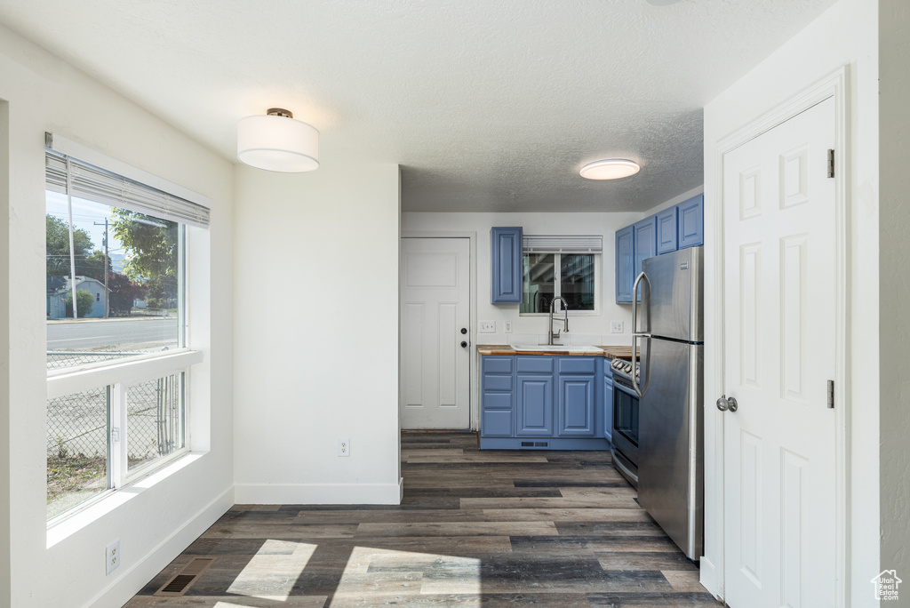 Kitchen with blue cabinets, appliances with stainless steel finishes, dark wood-style floors, and baseboards