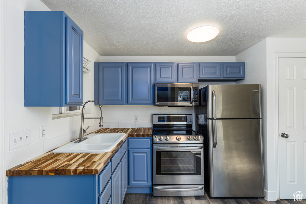 Kitchen featuring stainless steel appliances, a sink, blue cabinets, a textured ceiling, and dark wood finished floors