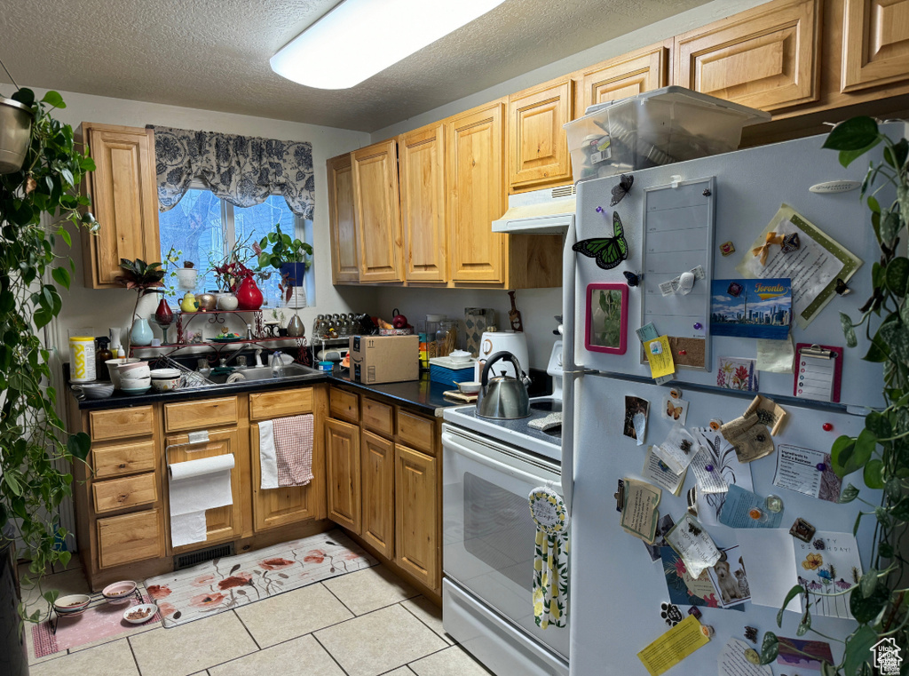 Kitchen with white appliances, under cabinet range hood, dark countertops, light tile patterned flooring, and a textured ceiling