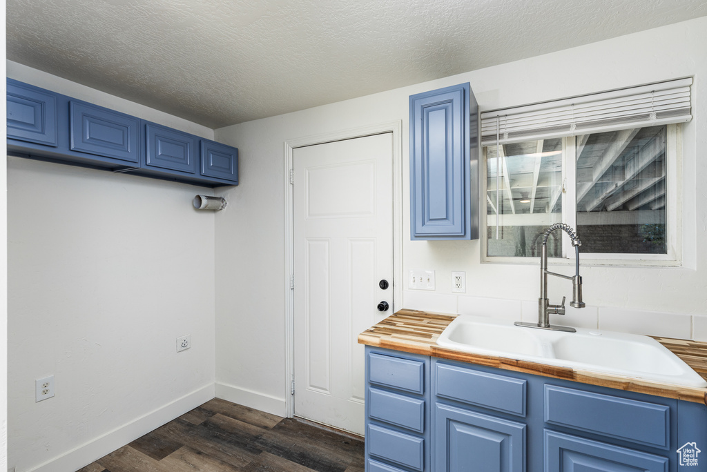 Kitchen with blue cabinetry, a sink, dark wood finished floors, baseboards, and a textured ceiling