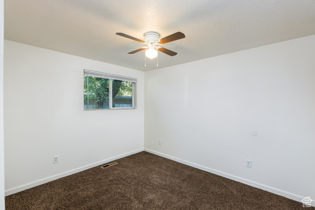 Spare room featuring ceiling fan, dark colored carpet, and baseboards
