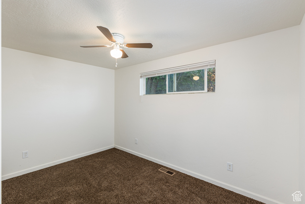 Unfurnished room featuring dark colored carpet, ceiling fan, and baseboards