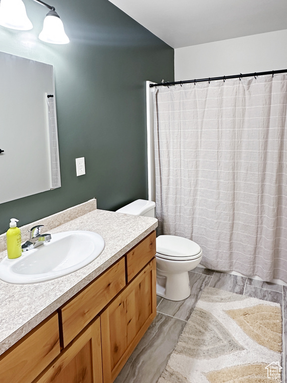 Bathroom featuring toilet, vanity, and curtained shower