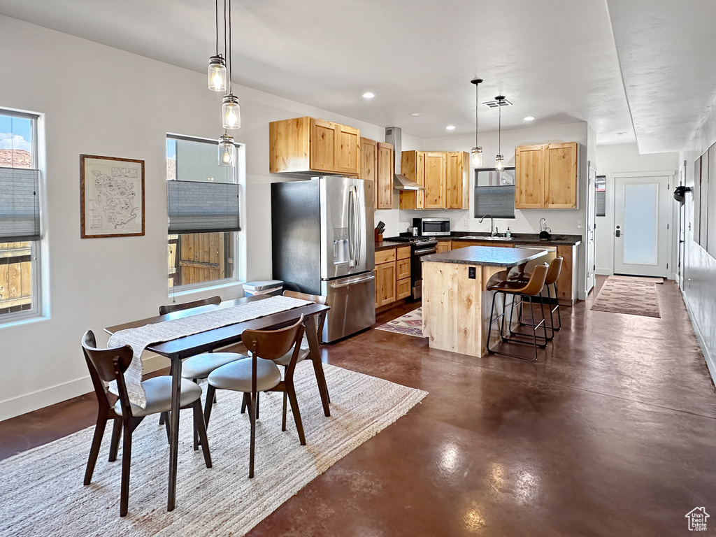 Kitchen featuring stainless steel appliances, a kitchen island, dark countertops, wall chimney exhaust hood, and finished concrete floors