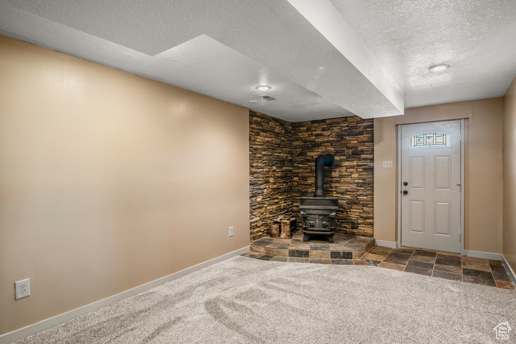 Unfurnished living room featuring a textured ceiling, baseboards, a wood stove, and carpet floors