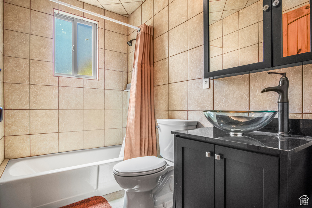 Bathroom with tile walls, shower / bath combo with shower curtain, toilet, vanity, and tasteful backsplash