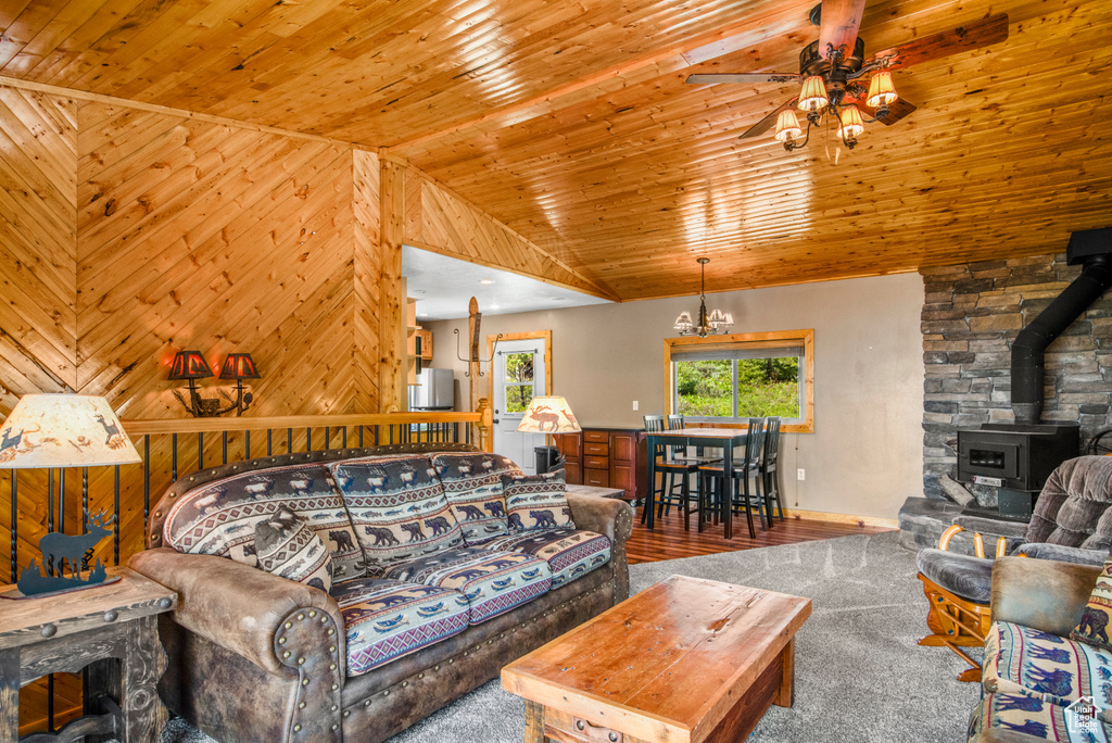 Living room with a ceiling fan, a wood stove, lofted ceiling, wooden ceiling, and carpet