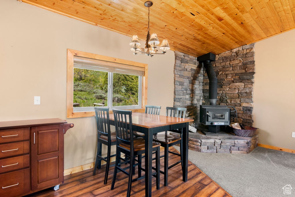 Dining area featuring a wood stove, a chandelier, wooden ceiling, wood finished floors, and baseboards