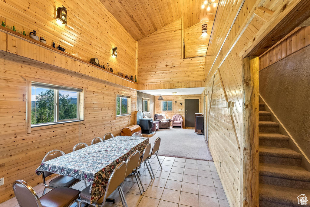 Dining room featuring high vaulted ceiling, wood walls, light tile patterned floors, light colored carpet, and wood ceiling