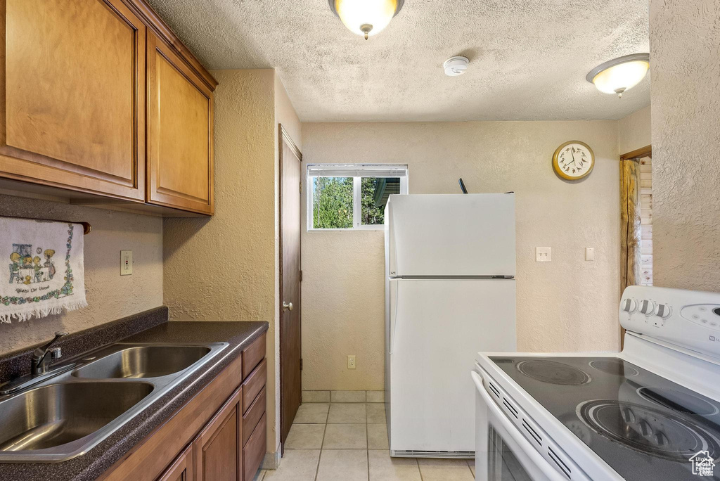 Kitchen featuring white appliances, a sink, brown cabinetry, a textured wall, and dark countertops
