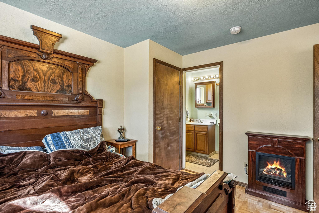 Bedroom featuring a glass covered fireplace, a textured ceiling, ensuite bath, and a sink