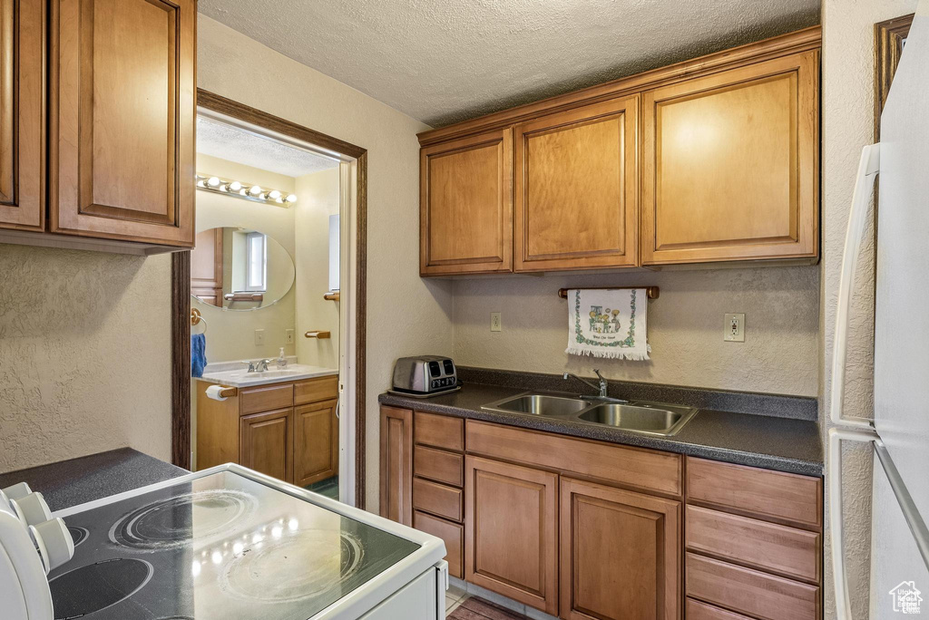 Kitchen with white appliances, a sink, brown cabinetry, a textured ceiling, and a textured wall